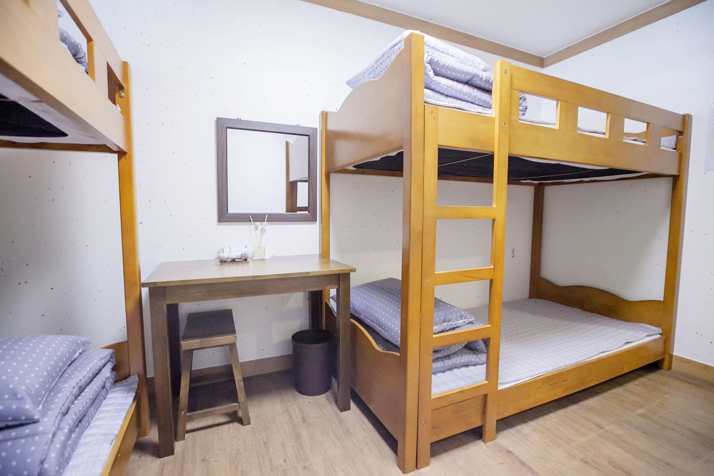 Une chambre avec un lit superposé, un bureau et une chaise, une petite poubelle et un miroir au mur.