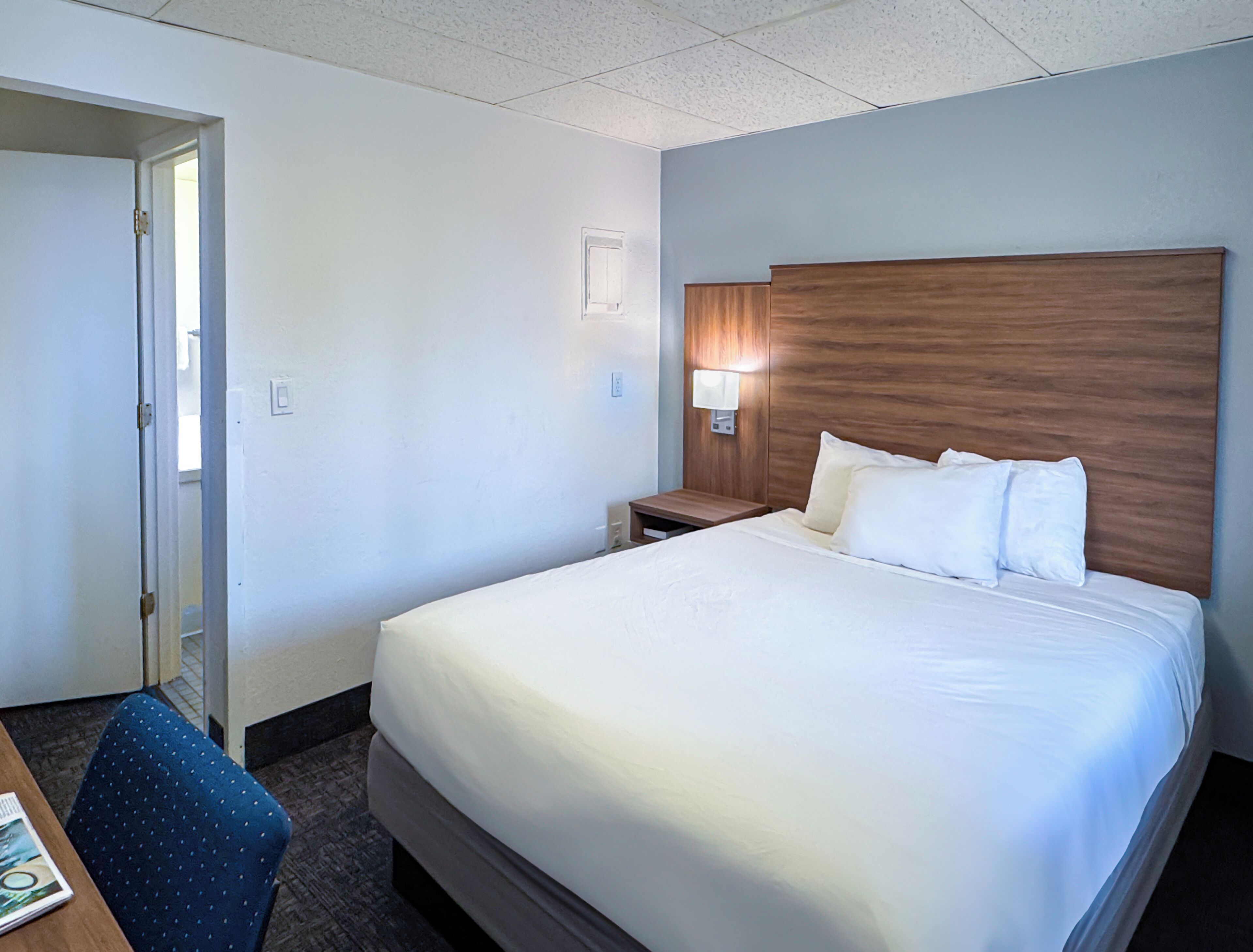 Una habitación de hotel con una cama grande, una mesita de noche, una lámpara, una silla y una puerta.