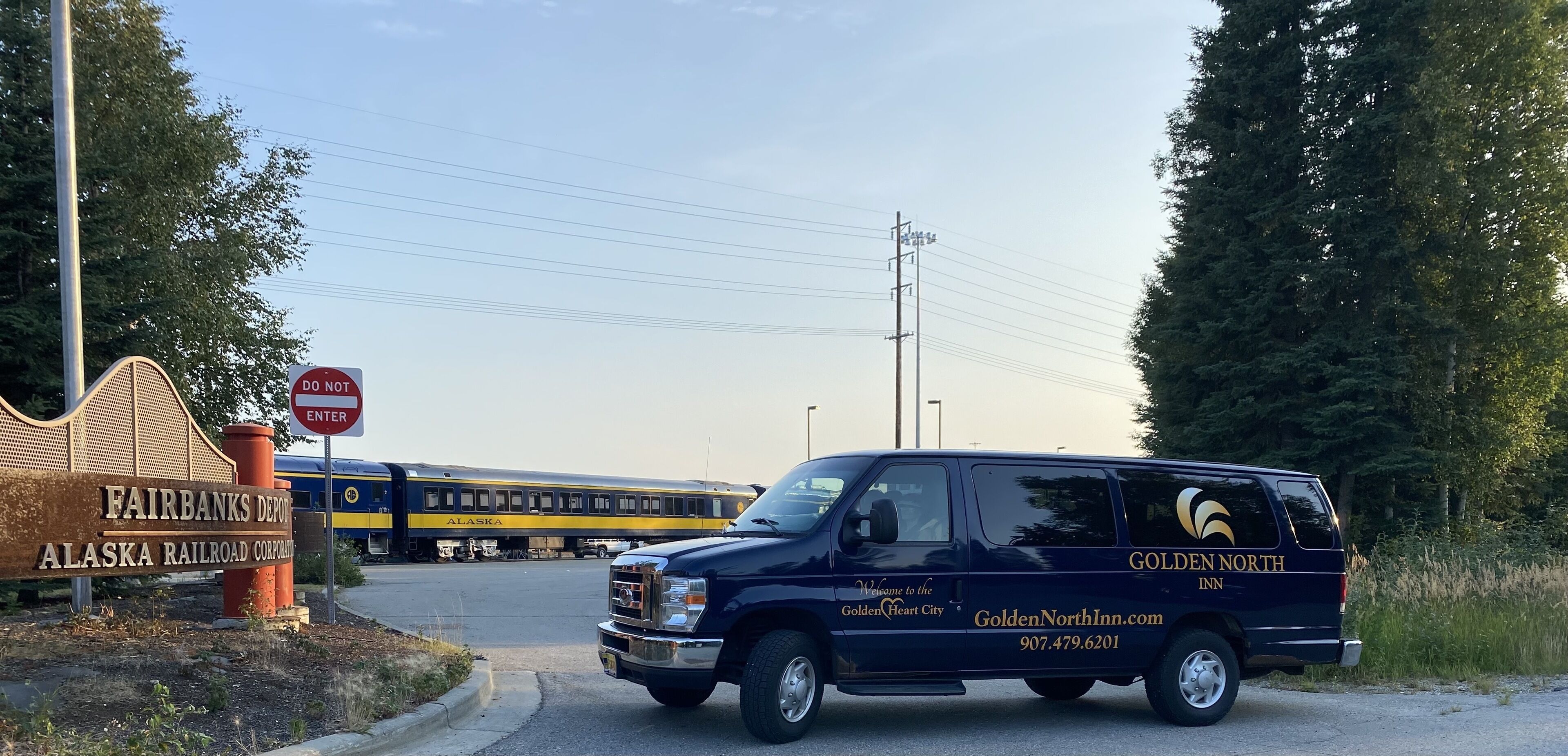 Una camioneta Golden North Inn estacionada cerca de una vía de tren, con un tren al fondo.