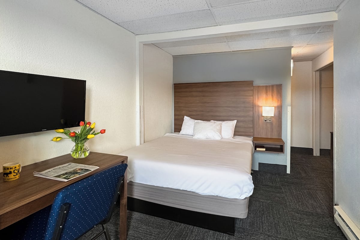 A hotel room with a bed, a desk with a chair, a television, and a lamp.