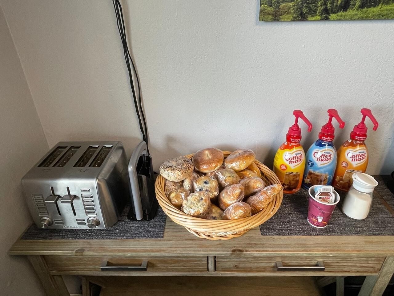 En køkkenbordplade med en brødrister, en kurv med rundstykker samt kaffeflasker og Nutella.