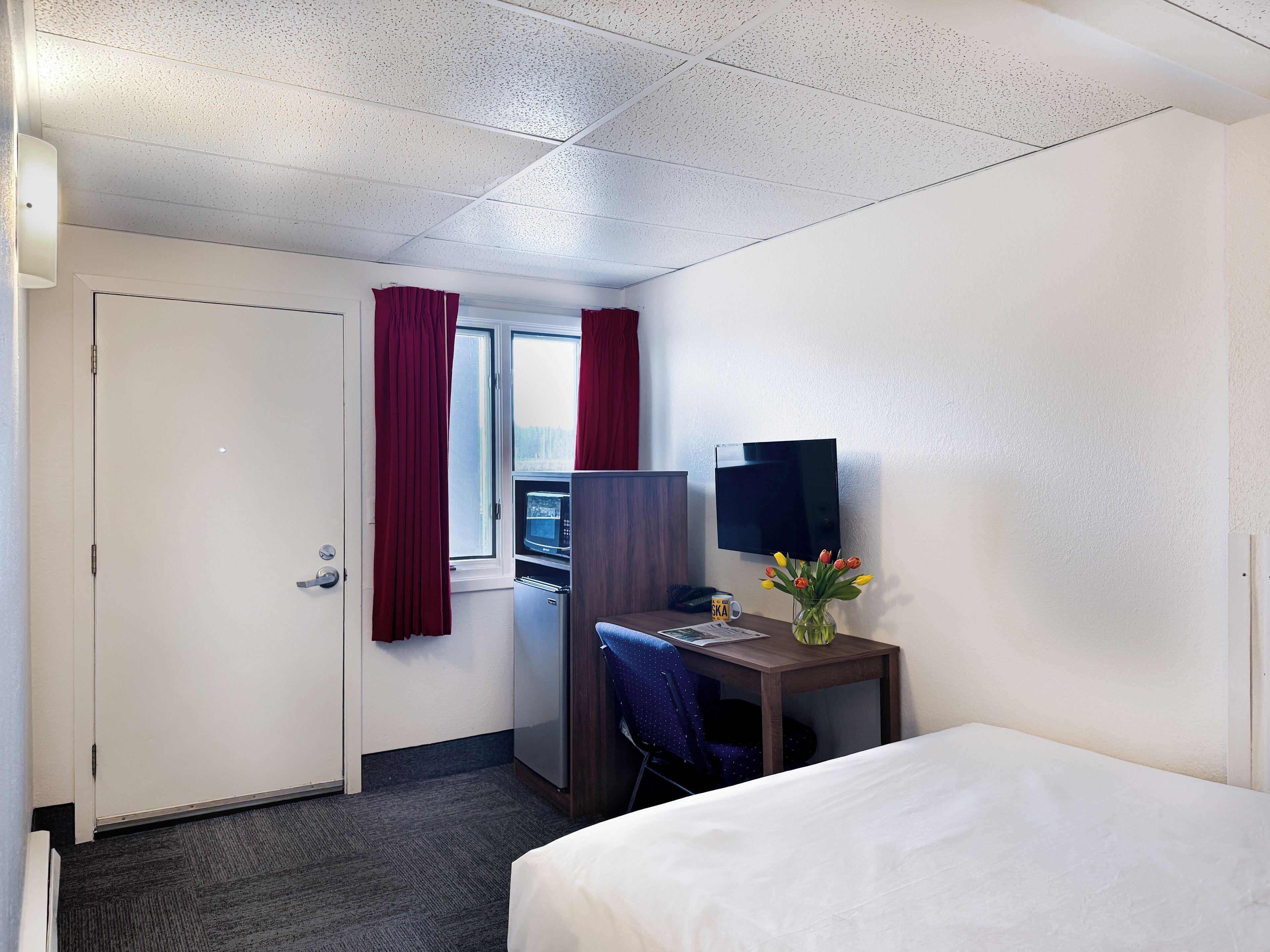 A hotel room with a bed, a desk with a computer, a TV, a microwave, and a window with curtains.
