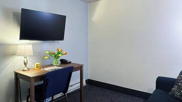 Ein Hotelzimmer mit Flachbildfernseher an der Wand, Schreibtisch mit Lampe, einer Vase mit Tulpen, Telefon und Stuhl.