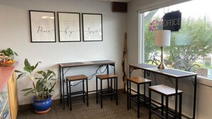 An office with a desk, two stools, a potted plant, framed inspirational quotes, and a window with a view of trees and a bicycle. - Golden North Inn (Fairbanks)
