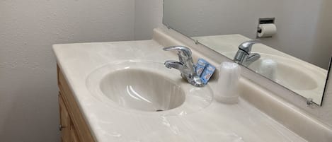 Ein Badezimmer mit einem weißen Waschbecken, zwei Wasserhähnen, einem Spiegel und Holzschränken.