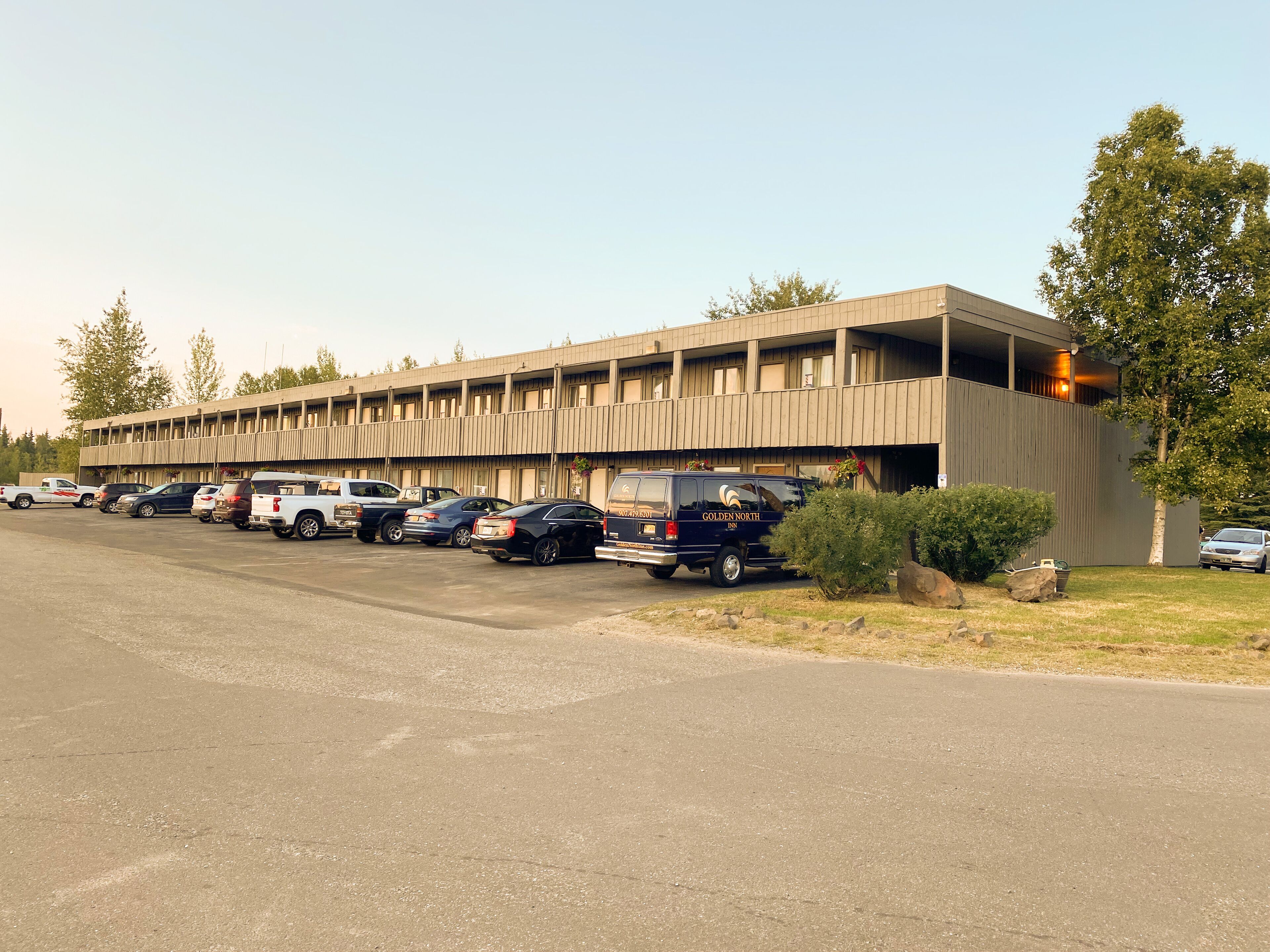 A multi-story motel with a row of parked vehicles in front.