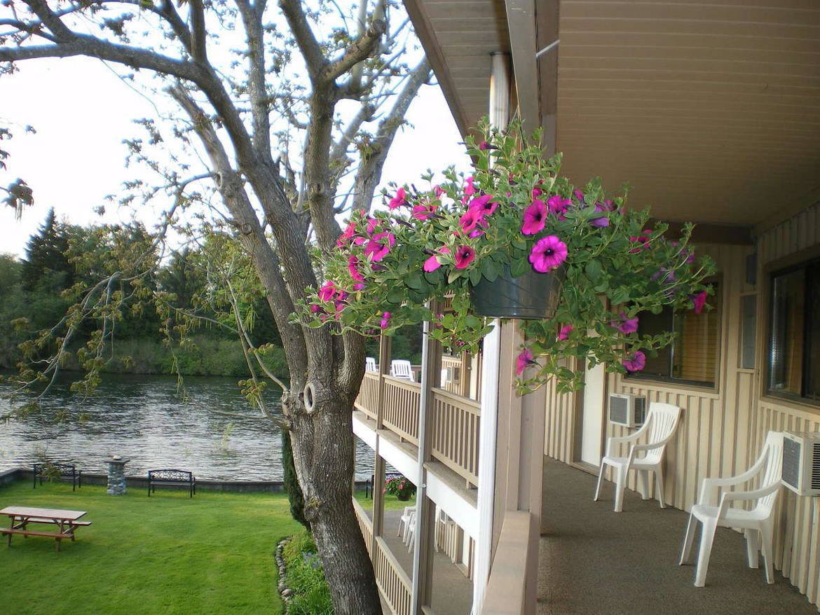 A hotel with a balcony overlooking a lake, featuring hanging flower baskets and outdoor seating.