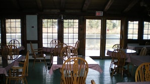 Comedor con sillas y mesas de madera, ventanas amplias con vistas a un cuerpo de agua y un letrero de salida.