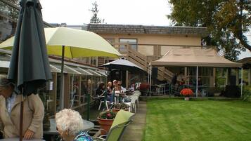 An outdoor seating area with tables and chairs, umbrellas, and a grassy lawn.