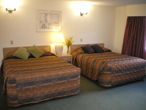 A hotel room with two beds, a nightstand with a lamp, a vase with flowers, and a painting on the wall. - Campbell River Lodge by Riverside (Campbell River)
