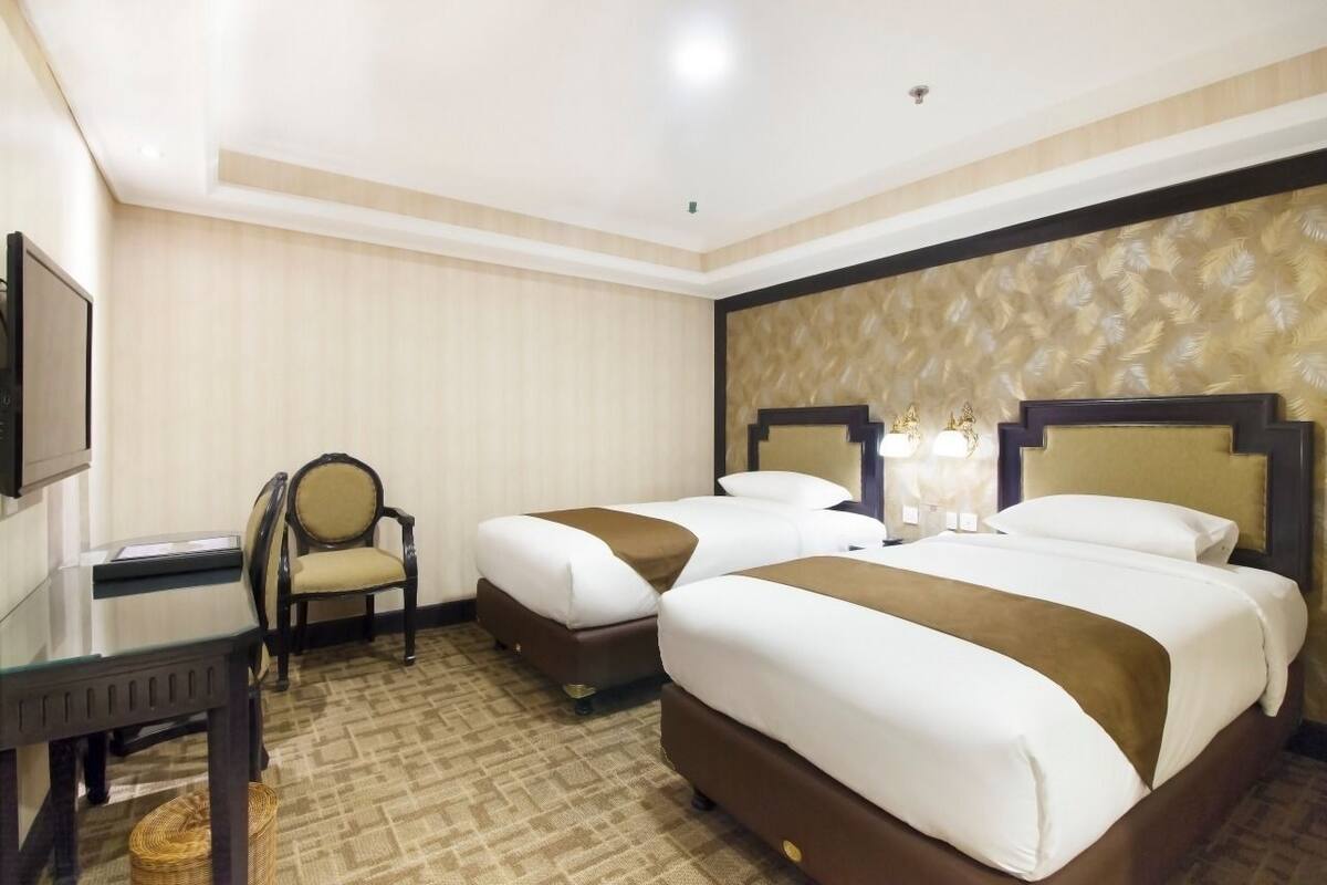 A hotel room with two beds, a desk, a chair, and a television.