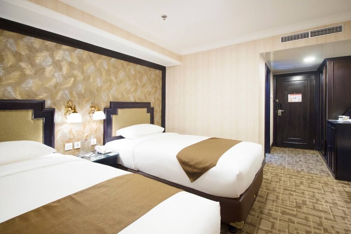 A hotel room with two beds, a wooden headboard, a desk with a lamp, and a door with a sign.