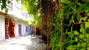 A narrow cobblestone street flanked by lush greenery and traditional architecture. - The Cave Studio Samui (Koh Samui)