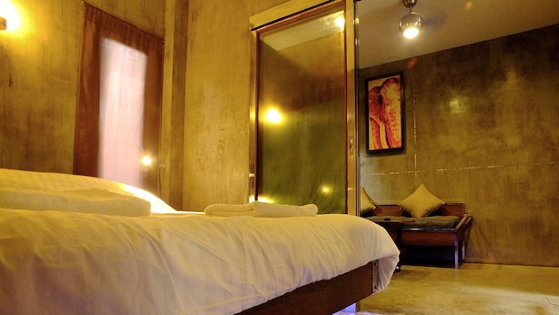 A modern hotel room with a large bed, a wooden nightstand, and a glass door leading to a bathroom. - The Cave Studio Samui (Koh Samui)