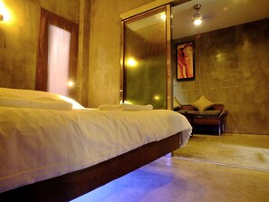 A modern hotel room with a large bed, a wooden nightstand, and a glass door leading to a bathroom. - The Cave Studio Samui (Koh Samui)