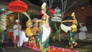 A traditional dance performance with participants in elaborate costumes, a red umbrella, and a decorated stage. - Rumah Desa (Marga)