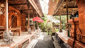 An indoor temple with intricate carvings, a central altar, and a red umbrella. - Rumah Desa (Marga)