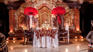 An ornate altar with intricate carvings and red umbrellas, surrounded by candles and a white cloth. - Rumah Desa (Marga)