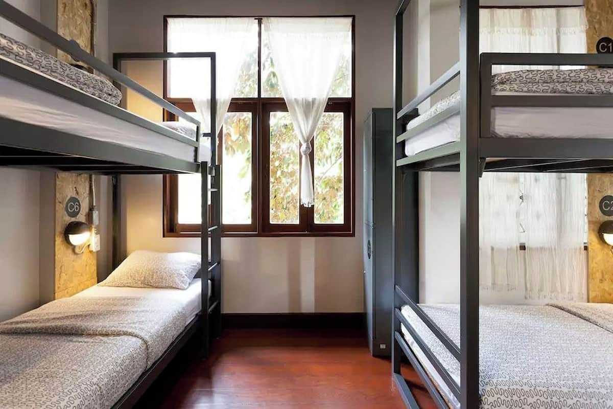 A room with bunk beds, a window with curtains, and a wall-mounted light fixture.