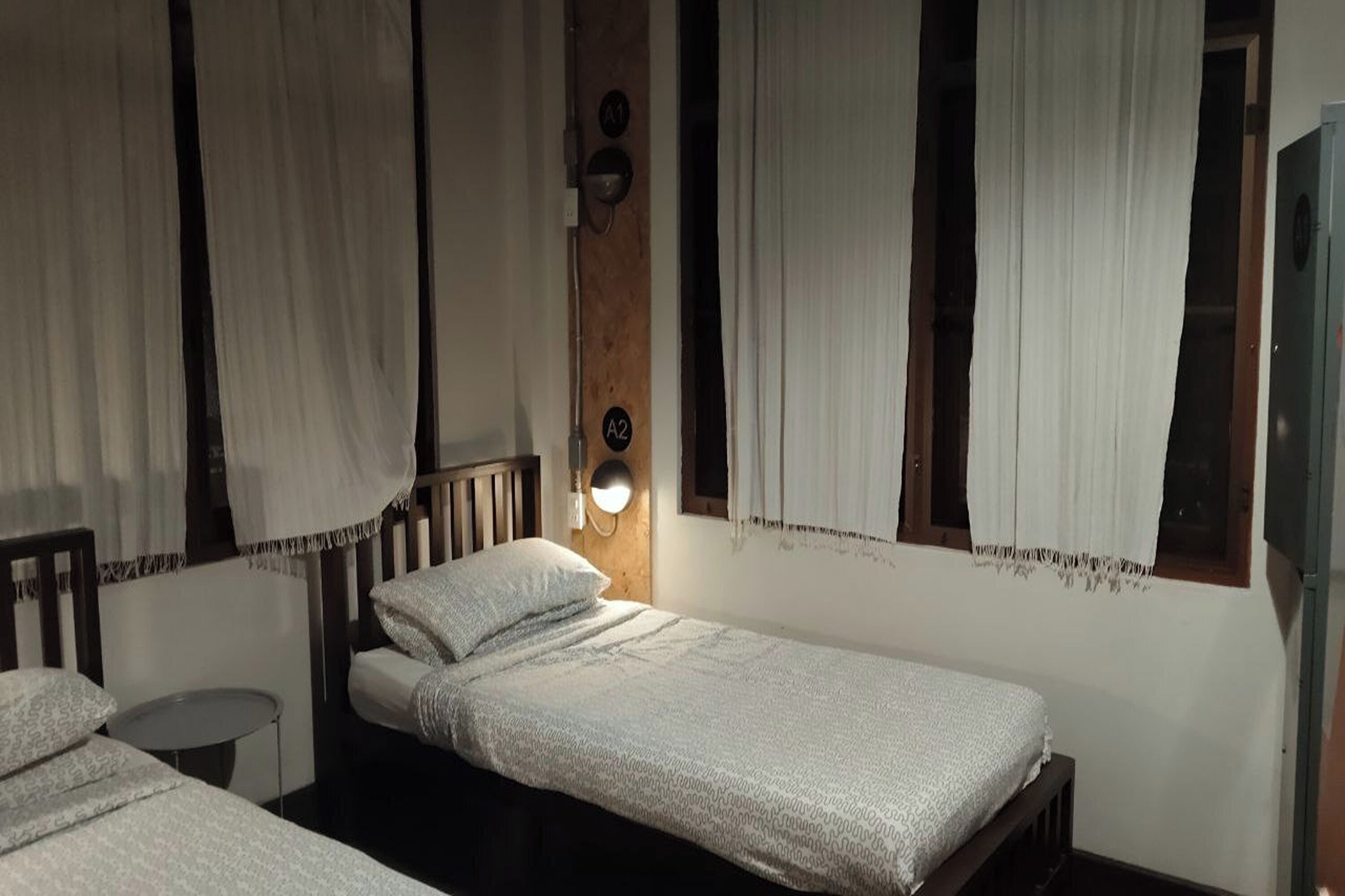 Ein Zimmer mit zwei Einzelbetten, einem kleinen runden Tisch und einer Wandleuchte.