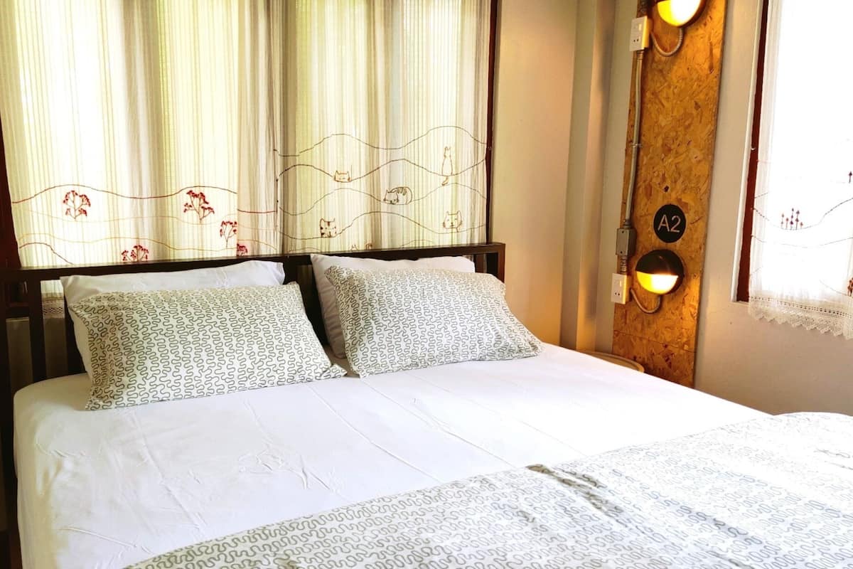A hotel room with a bed, a nightstand, a wall-mounted light, and a window with curtains.