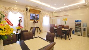 Comedor de hotel con una mesa grande, sillas, televisor y dispensador de agua.