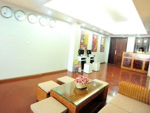 A reception area with a reception desk, computers, and a wall clock. There are cushioned seating areas and a glass-top table with a flower vase.