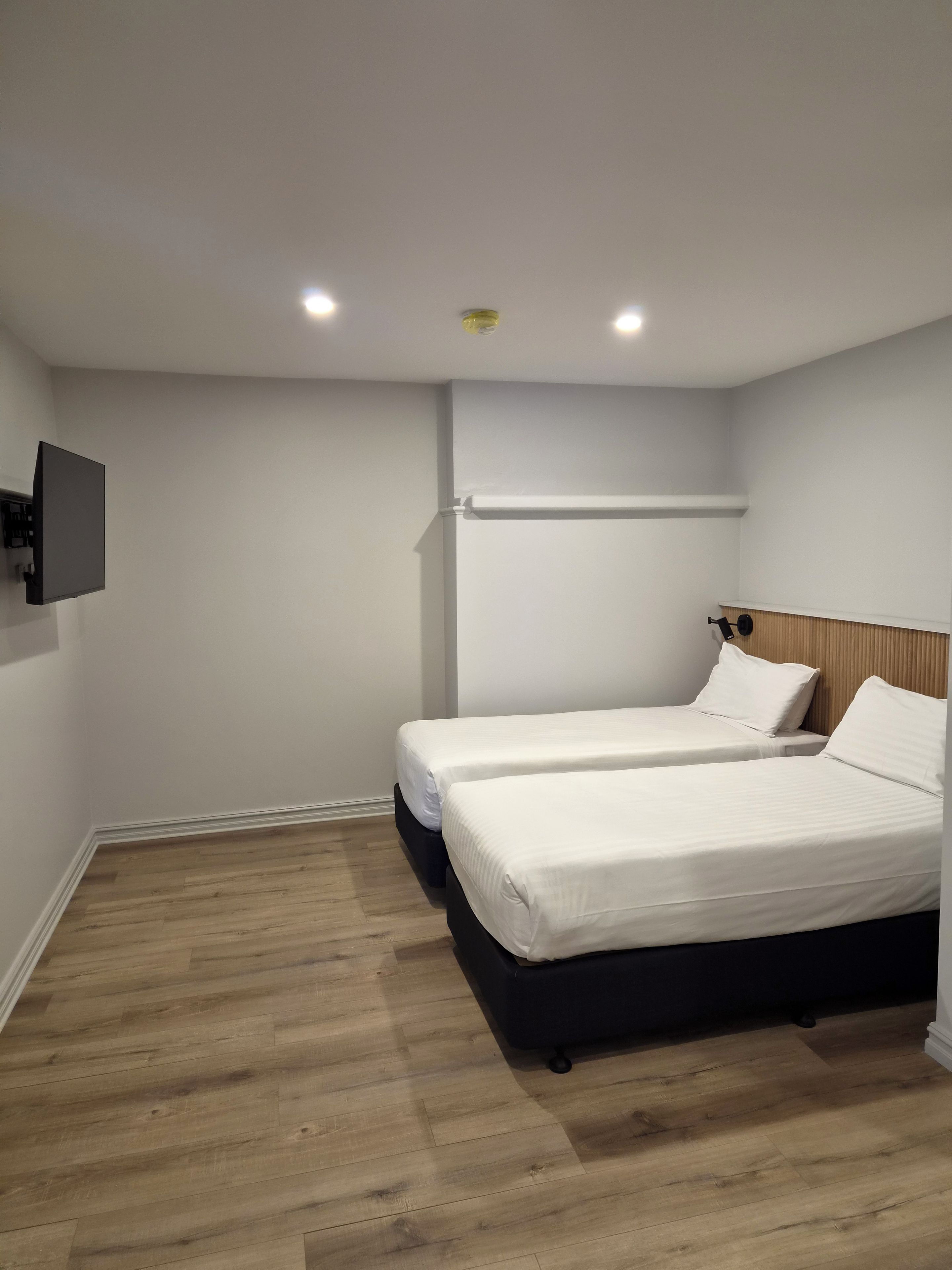 Une chambre avec deux lits, un téléviseur fixé au mur et un plancher en bois.