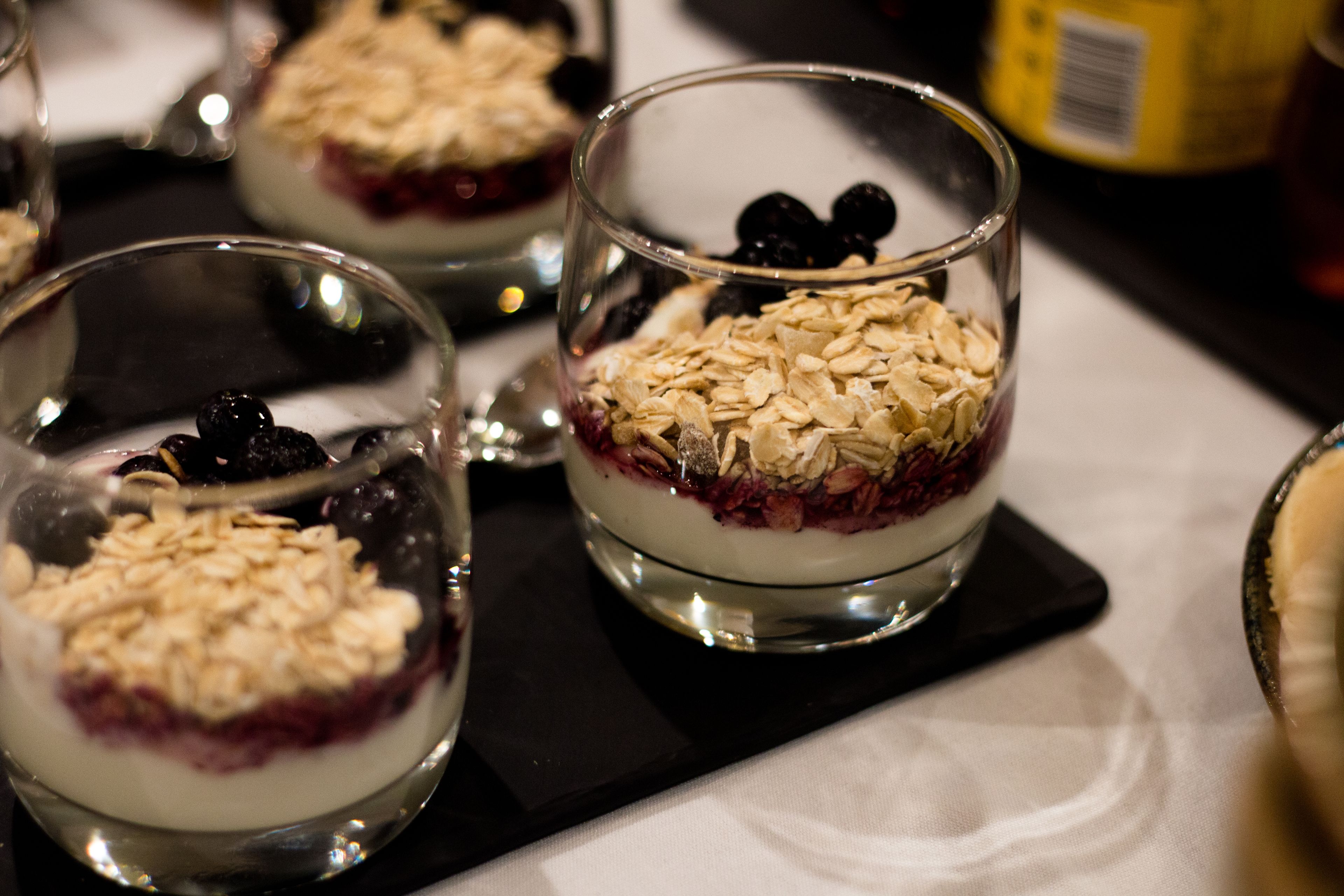 Three glasses of dessert with oats and berries on a black tray.
