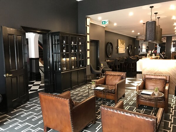 Un área de bar moderna con sillones de cuero, suelo de cuadros y una vitrina para vinos.