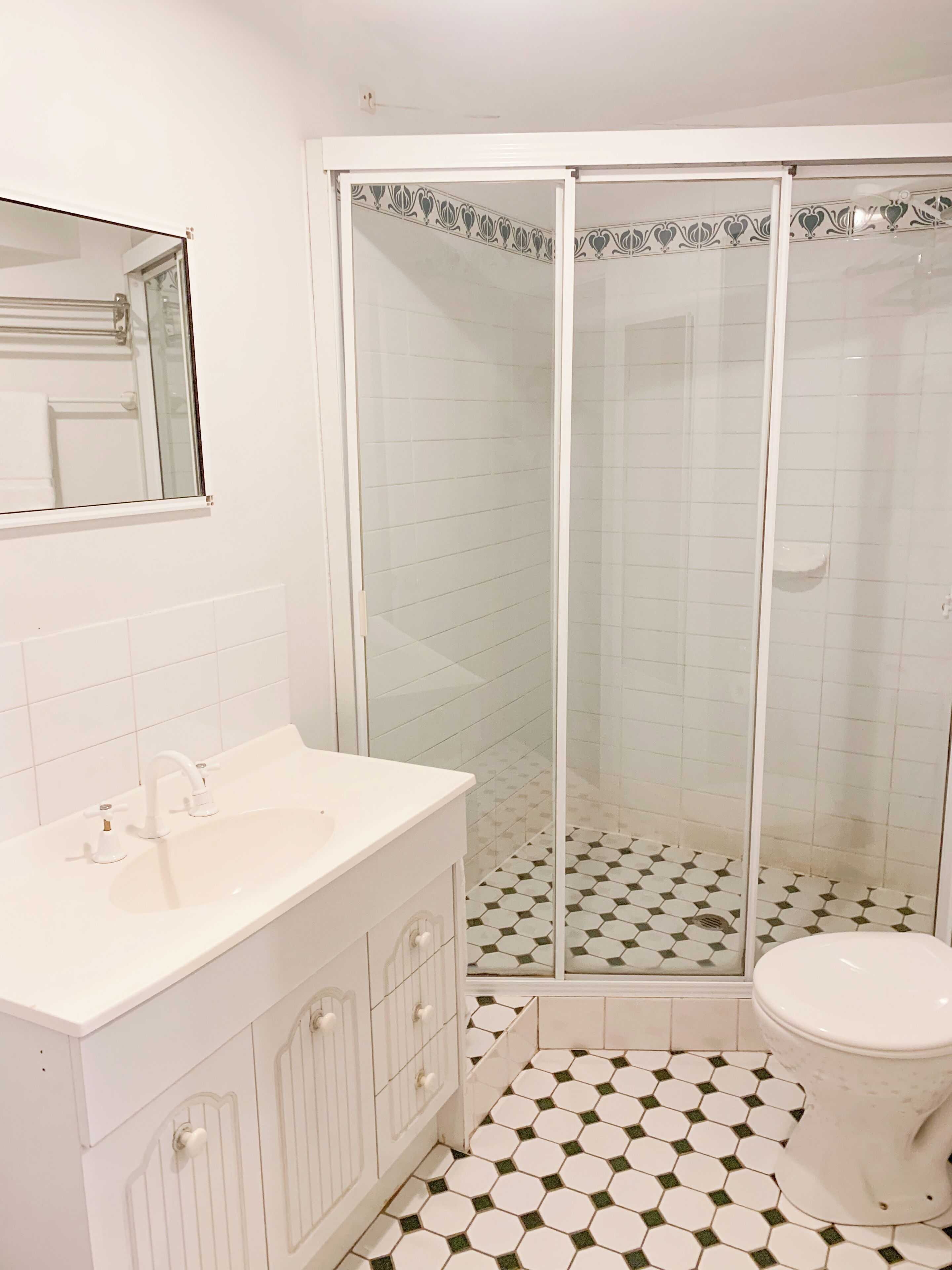Une salle de bain avec un lavabo blanc, des toilettes et une douche en verre, le sol étant recouvert de carreaux à motifs.