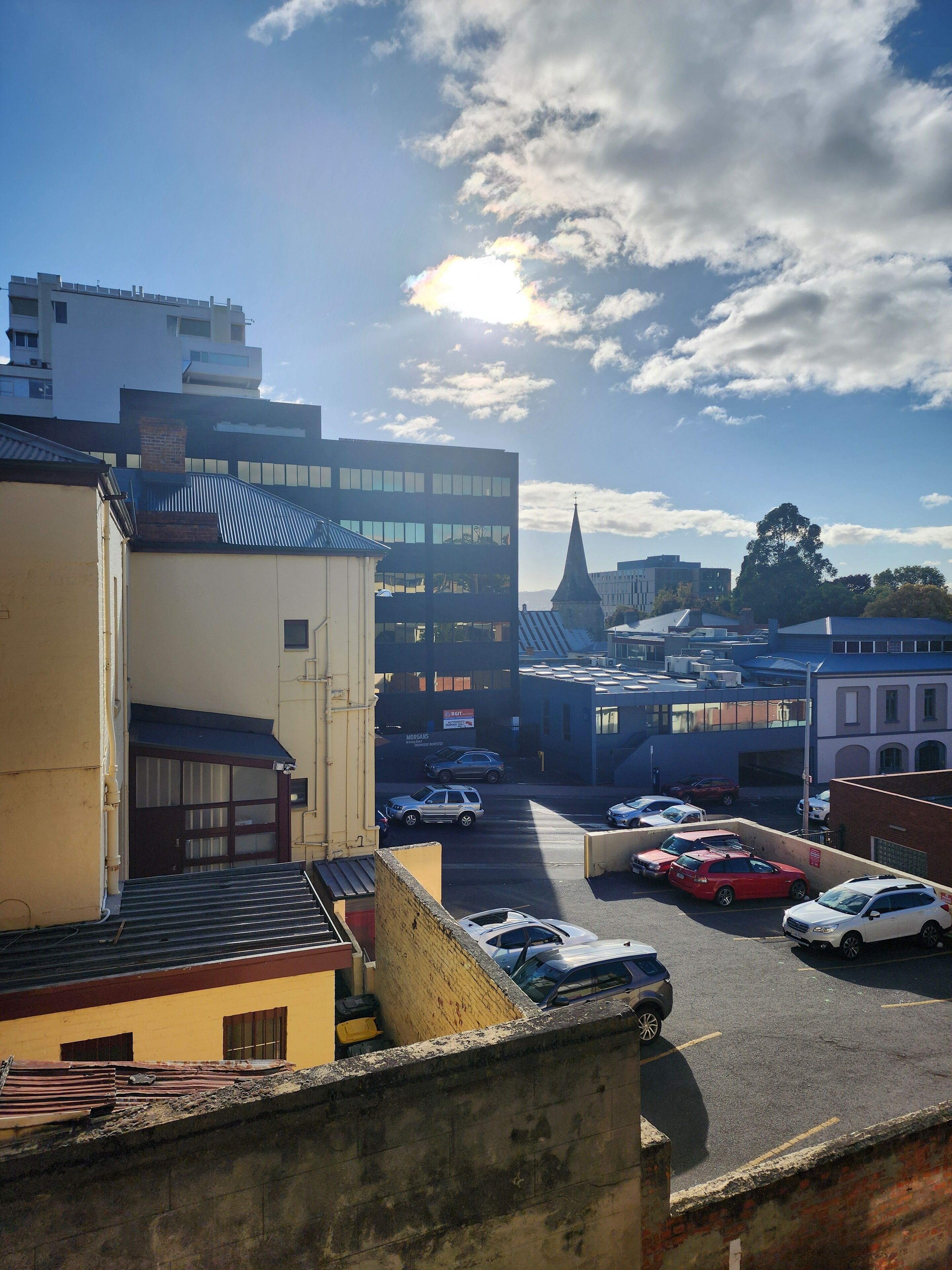 A parking lot with several cars, a church with a pointed steeple, and modern buildings in the background.