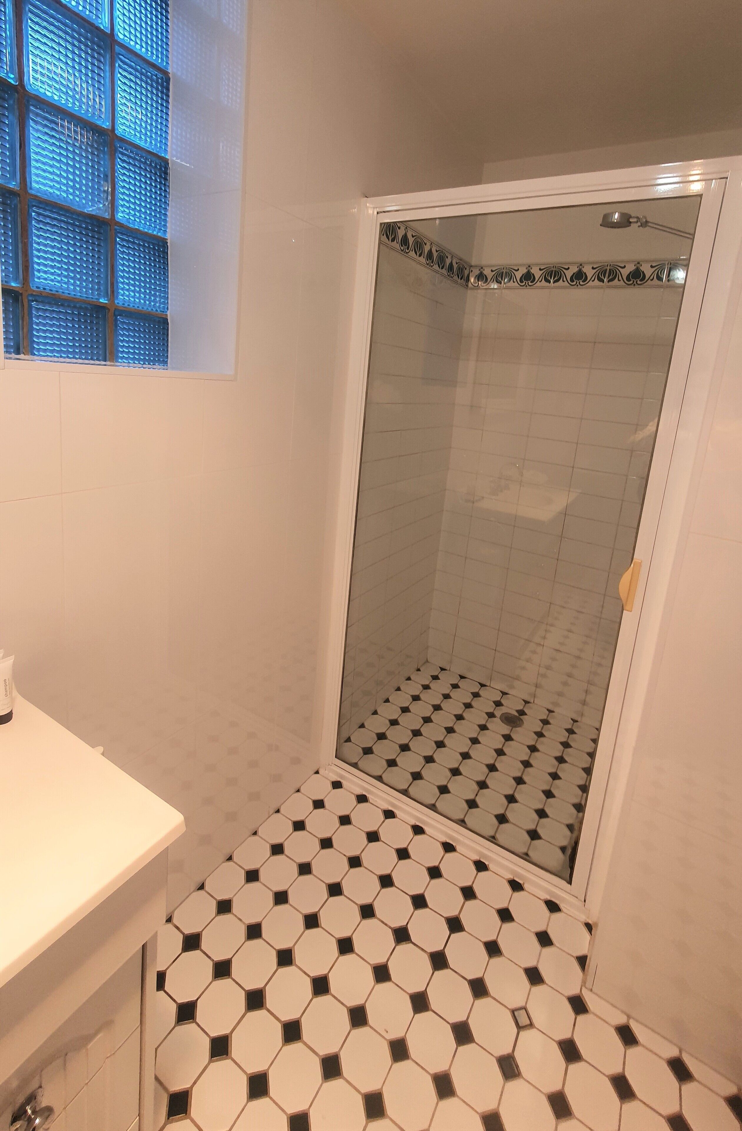 A bathroom with a shower, tiled floor, and a window with blue-tinted glass.