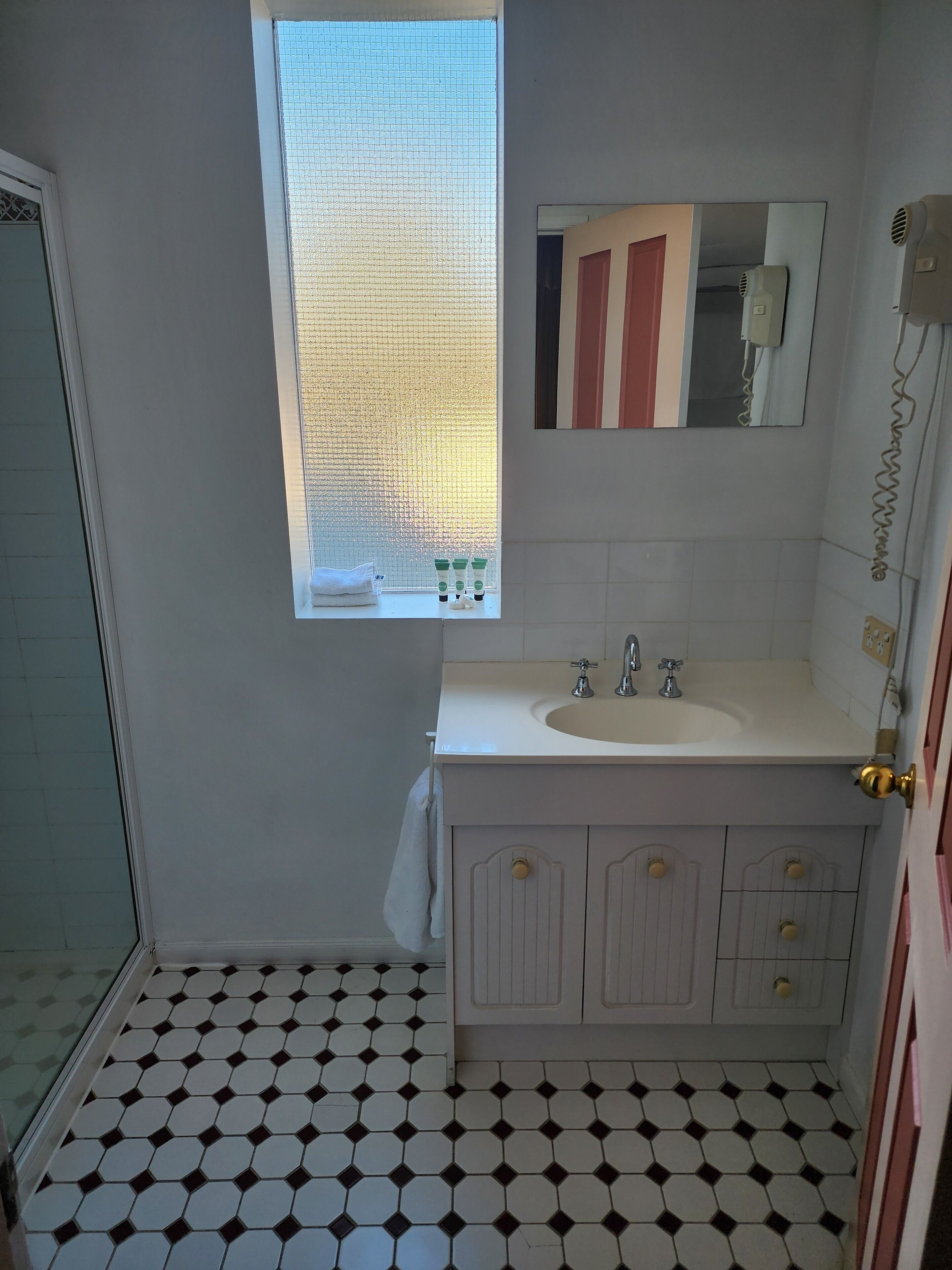 A bathroom with a white sink, two faucets, a mirror, and a window with a view of the outside.