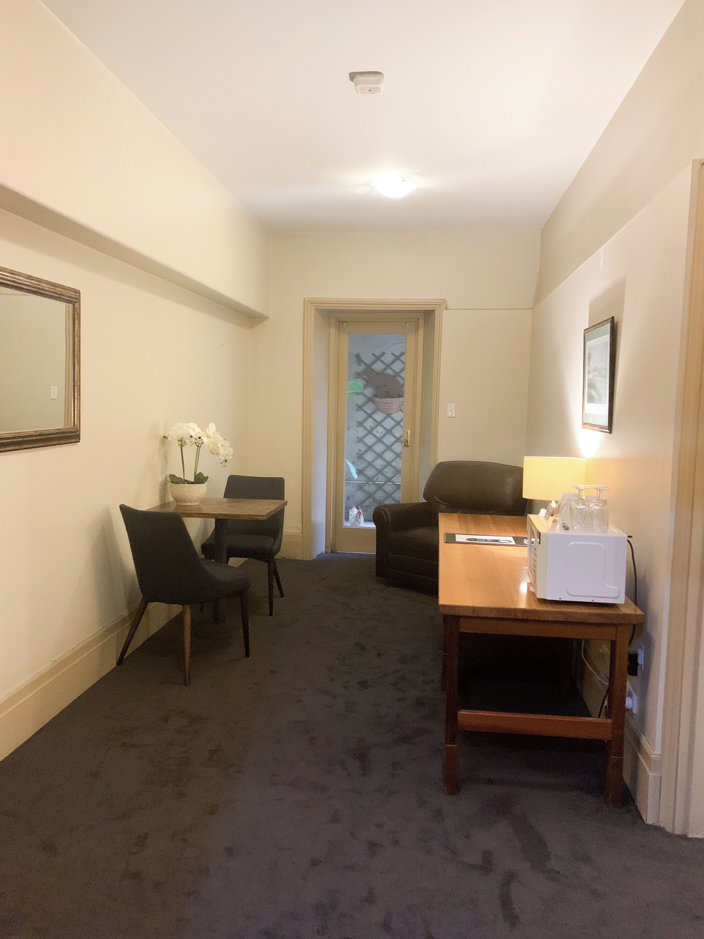 A compact living room with a dining area, a small table with a microwave, and a door leading to another room.