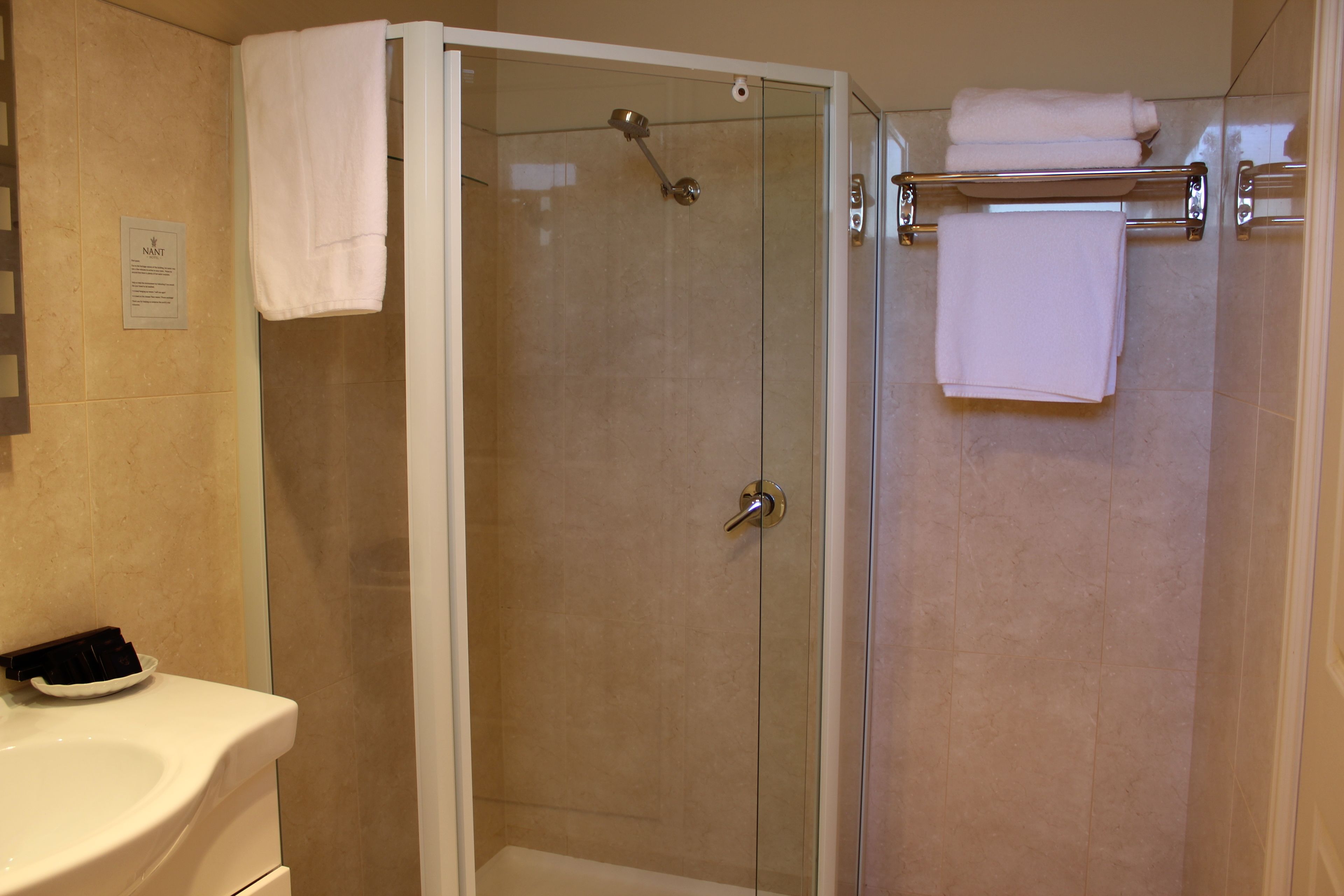 Un baño moderno con ducha de vidrio, lavamanos blanco y toallero con toallas dobladas.