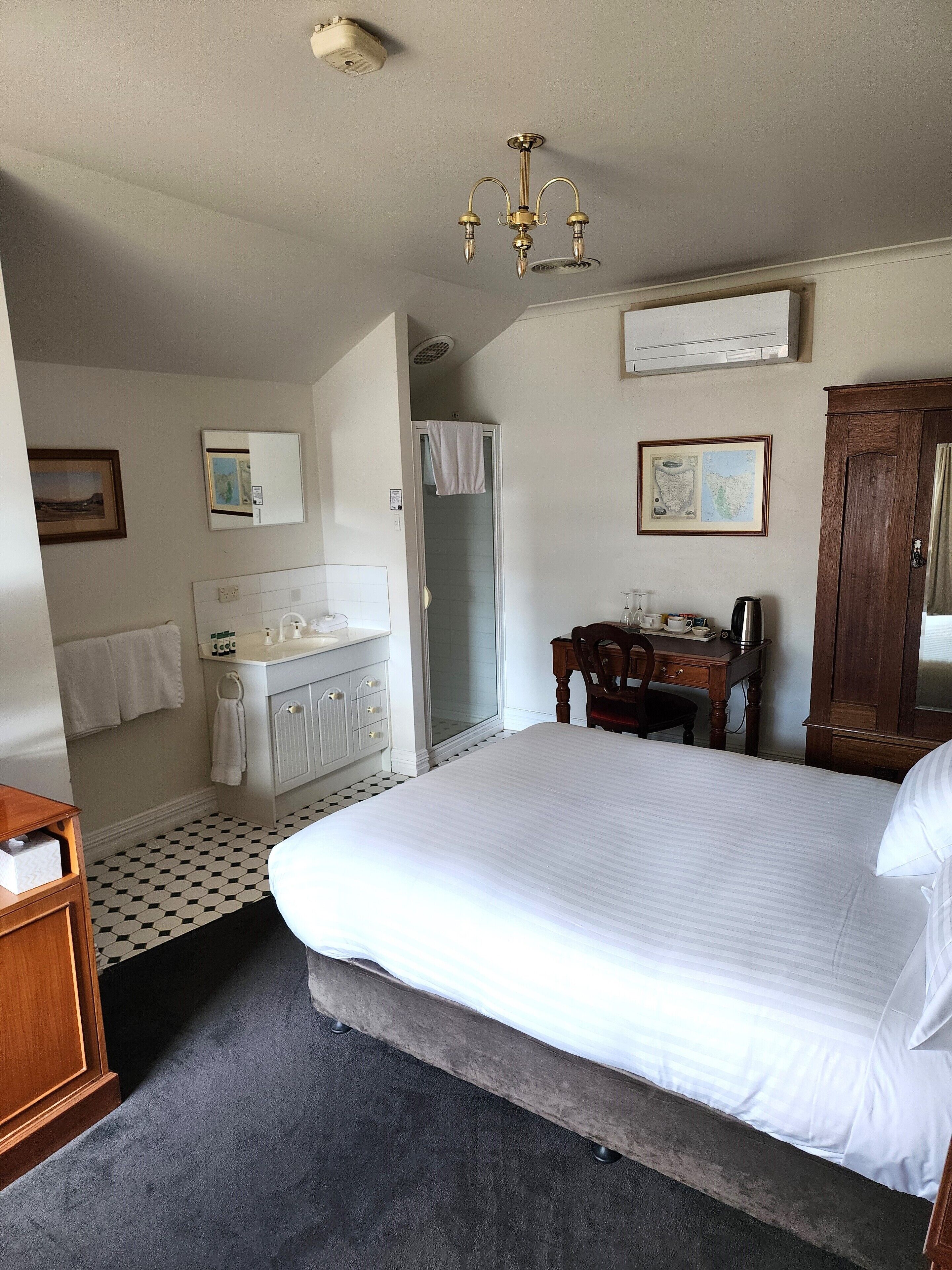 A hotel room with a large bed, a bathroom with a sink and mirror, a wooden desk, and a map on the wall.