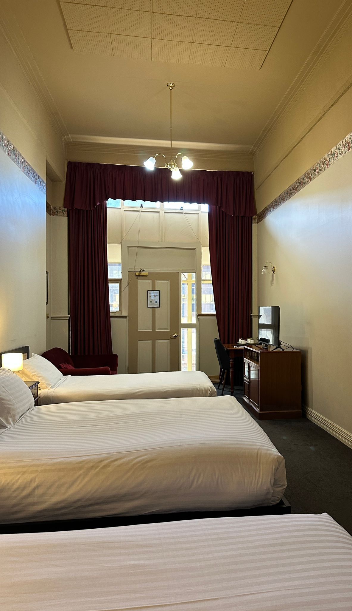 A hotel room with two beds, a desk with a chair, a television, and a window with curtains.