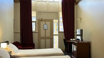 A hotel room with two beds, a desk with a chair, a television, and a window with curtains.