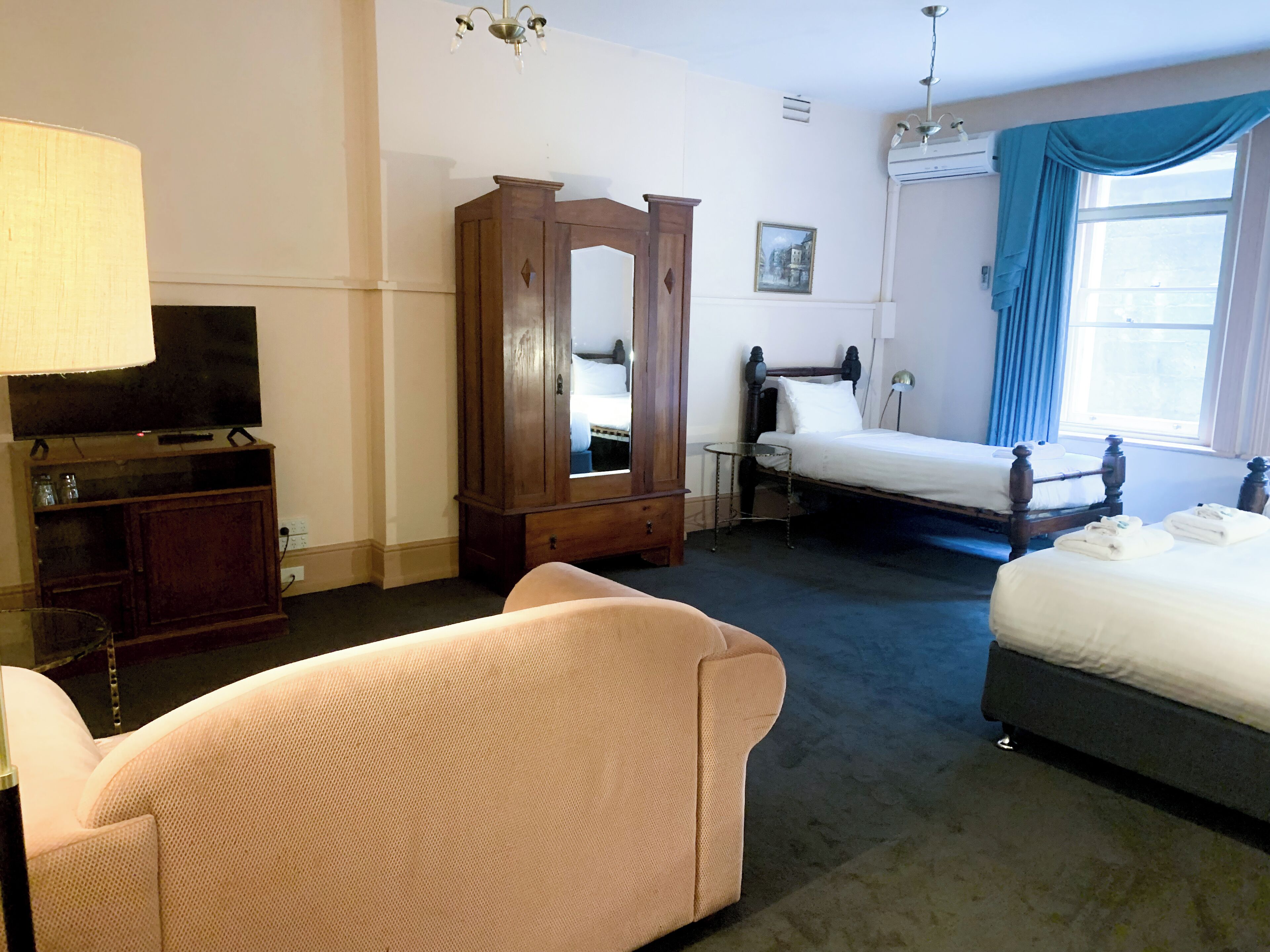 A hotel room with a bed, a sofa, a TV, a wardrobe, and a mirror.