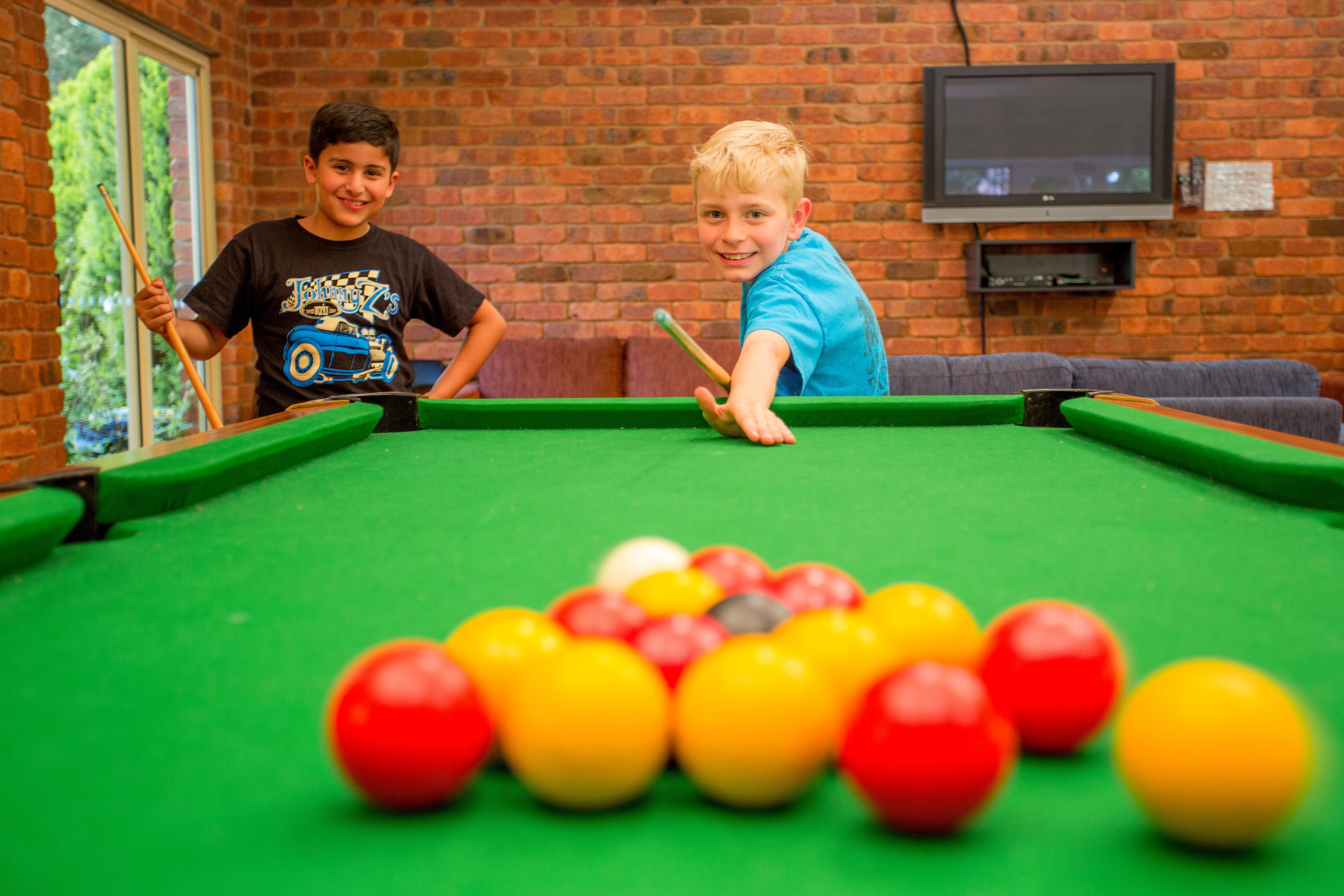 A pool table with balls in a room with brick walls and a television mounted on the wall.