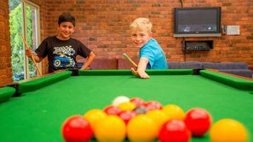 A pool table with balls in a room with brick walls and a television mounted on the wall.