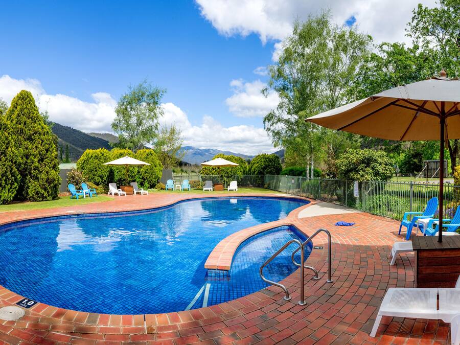 Une piscine bordée de briques, entourée de chaises et de parasols bleus, et offrant une vue sur les arbres et les montagnes en arrière-plan.