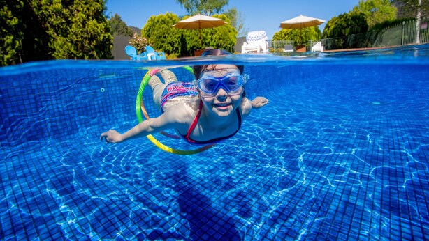 A swimming pool with clear blue water, a swimmer in the foreground, and umbrellas in the background. - Discovery Parks - Bright (Freeburgh)