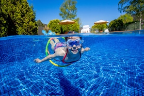 Ein Schwimmbecken mit klarem, blauem Wasser, ein Schwimmer im Vordergrund und Sonnenschirme im Hintergrund.