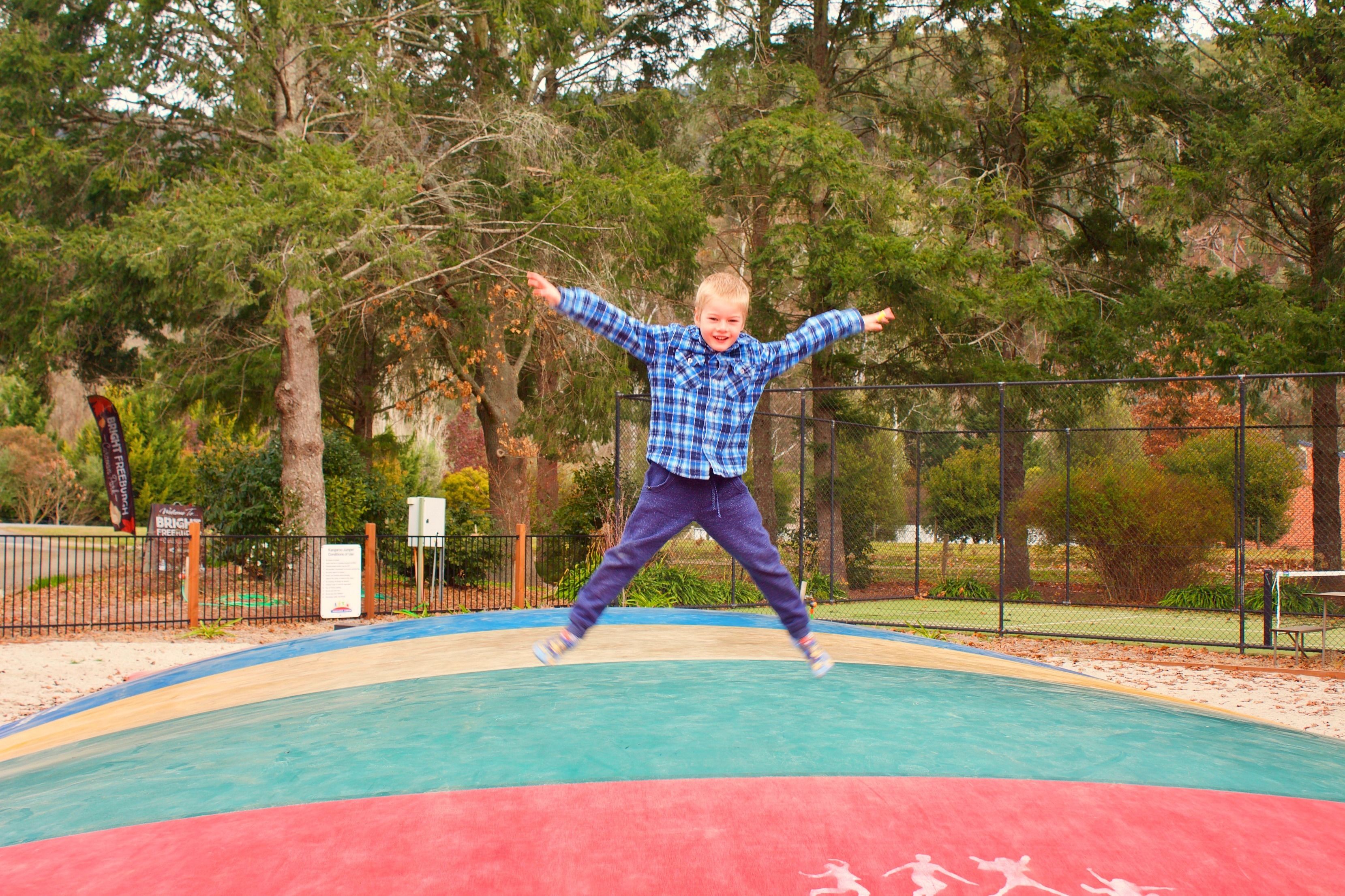 A child jumping on a trampoline in an outdoor area with trees and a fence in the background.
