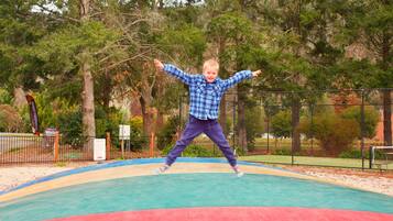 Niño saltando en un trampolín en un espacio al aire libre con árboles y una valla de fondo.