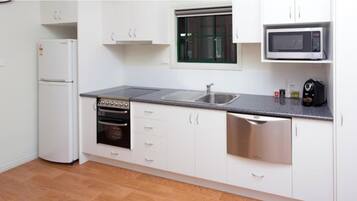 Una cocina compacta con armarios blancos, horno integrado, microondas y lavavajillas.