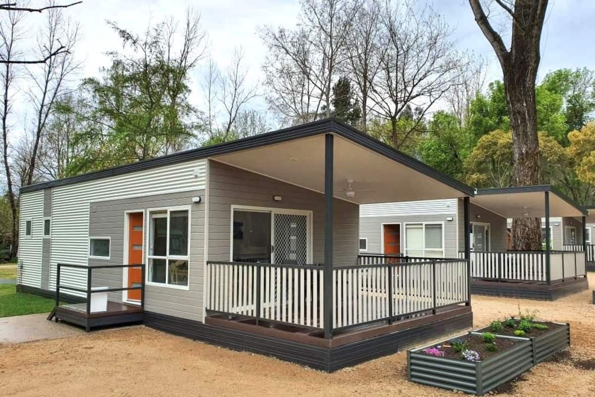 A single-story mobile home with a covered porch, a fenced yard, and a small garden area.