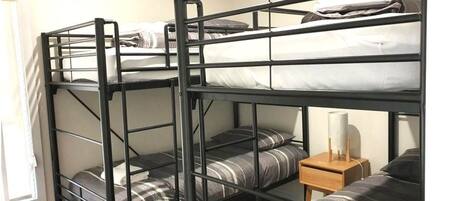 A bunk bed room with three levels, a small wooden nightstand, and a window.